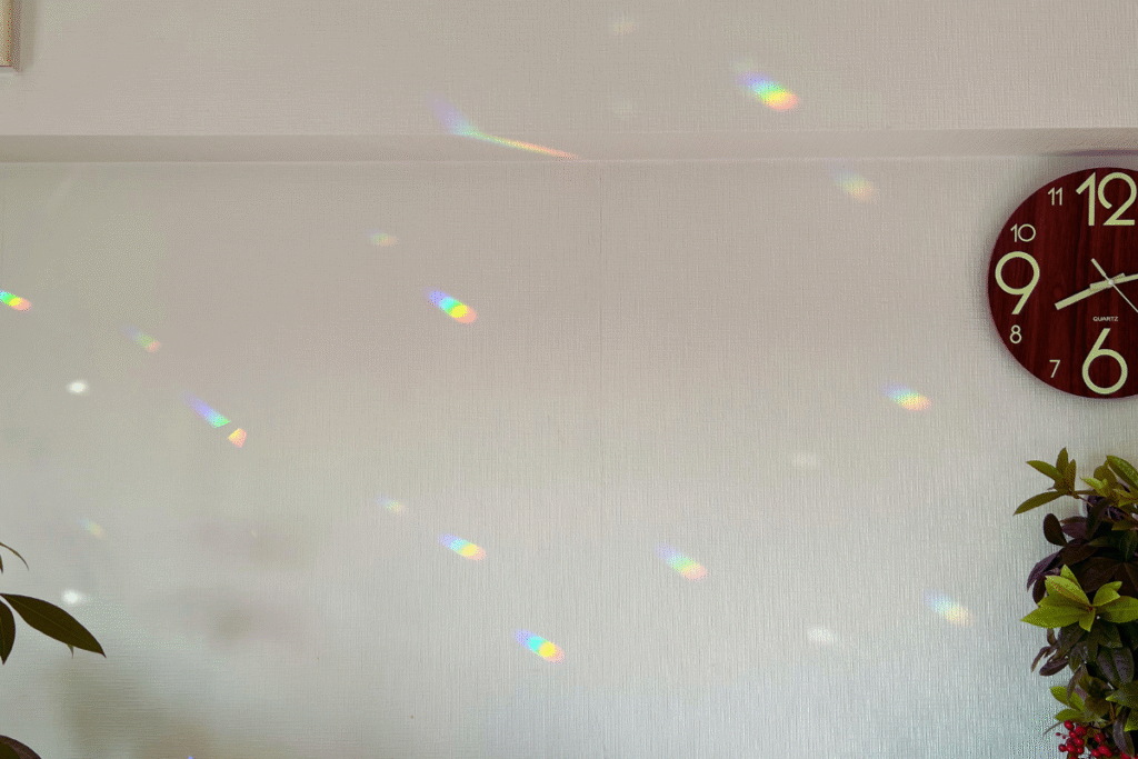 カーテンや壁に映る虹のプリズムが部屋いっぱいに広がるサンキャッチャーの光